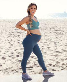 a woman is standing on the beach in her blue sports bra and leggings