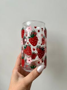 a hand holding up a glass with strawberries on it and hearts painted on the side