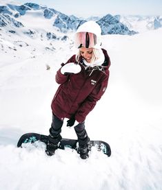 a woman riding a snowboard on top of a snow covered slope with mountains in the background