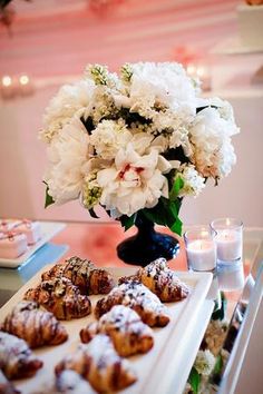 white flowers and pastries are on a table in front of a vase with candles