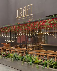 the outside of a restaurant with tables and chairs covered in hanging lights, plants and flowers