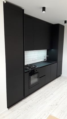 an empty kitchen with black cabinets and white tile on the walls, along with wood flooring