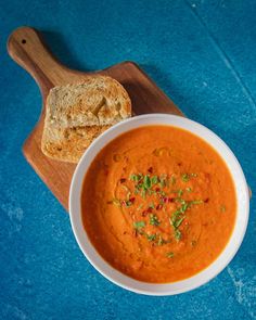 a bowl of tomato soup and a piece of bread on a cutting board next to it