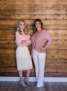 two women standing next to each other in front of a wooden wall