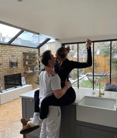 a man and woman hug in front of a kitchen sink while holding their arms around each other