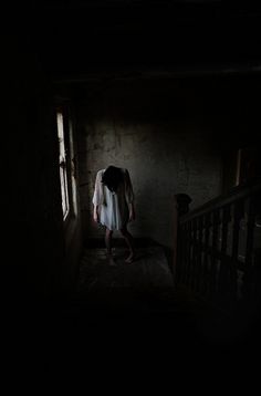 a person standing in the dark with their head down and hands behind her back,