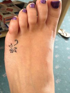 a woman's foot with a small flower tattoo on her left toe and purple nail polish