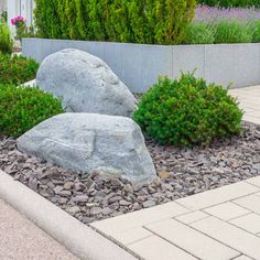 a garden with rocks and plants in front of a white house on a sunny day