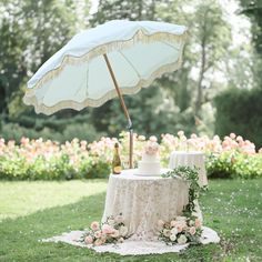 a table with an umbrella and cake on it in the middle of some grass near flowers