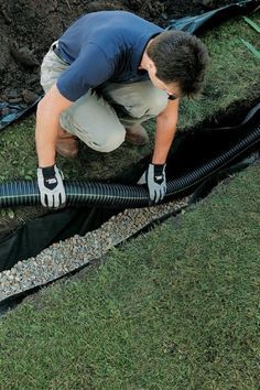 a man is working on a drainage system in the grass with his hands and gloves