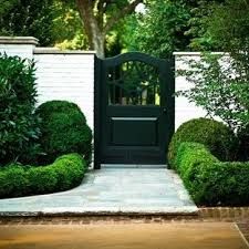 a black door is in the middle of a garden with bushes and trees around it