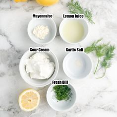 the ingredients to make lemonade are shown in bowls on a marble counter top with lemons, sour cream, garlic salt, fresh dill and mayonnaise