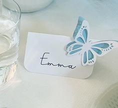 there is a place card with a butterfly on it and water in the glass next to it