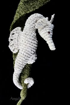 a crocheted seahorse is shown in white and green, on a black background