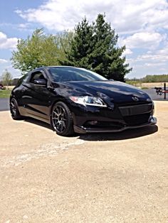 a black sports car parked in a parking lot next to a park bench and trees