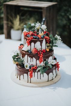 a three tiered cake with berries and chocolate icing sitting on a white table