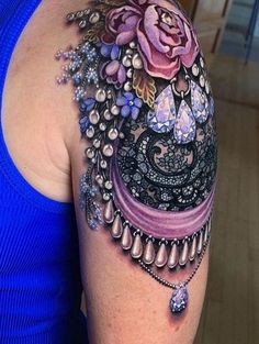 a woman with a tattoo on her arm has a blue top and purple flowers in the background