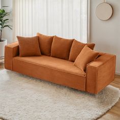 an orange couch sitting on top of a rug in front of a white wall and window