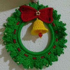 a green wreath with a red bow and a bell hanging from the side on a wall