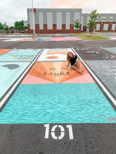 a woman sitting on the ground in front of a painted parking lot with an umbrella