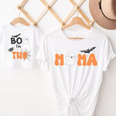 two halloween t - shirts hanging on a clothes rack