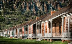 an old row of houses in front of a mountain range with trees and mountains behind them