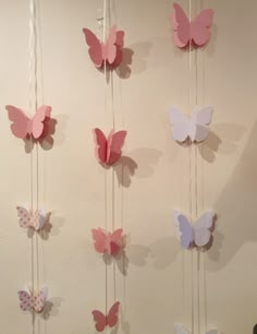 several pink and white butterflies hanging from strings on a wall next to a black cat