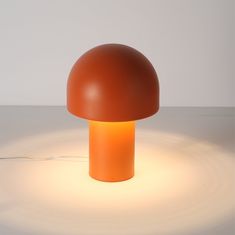 an orange mushroom lamp sitting on top of a white table next to a light bulb