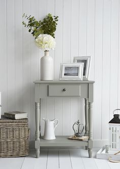 a white vase with flowers sitting on top of a table next to a wicker basket