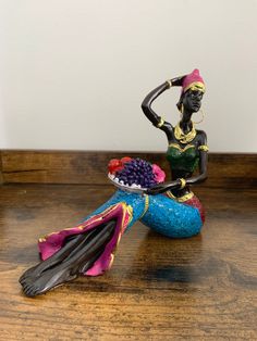 a figurine sitting on top of a wooden table holding a bowl of grapes