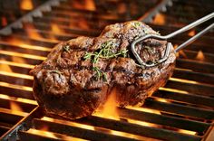 steak on the grill being grilled with tongs and garnished with herbs