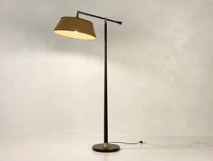 a floor lamp with a brown shade on the base and a white wall behind it