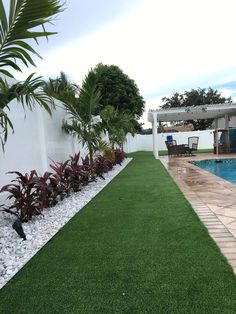 a backyard with artificial grass and plants next to a swimming pool