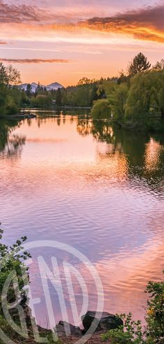 the sun is setting over a lake with mountains in the distance and trees around it