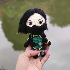 a hand holding a small crocheted doll with black hair and beard wearing a green shirt