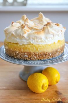 a lemon meringue pie sitting on top of a cake plate next to two lemons