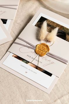 the wedding stationery is adorned with a wax stamp and a feather ornament