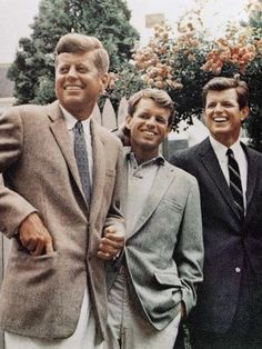 three men standing next to each other in front of a white picket fence and flowers