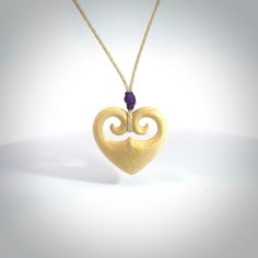 a wooden heart shaped pendant with a purple bead hangs from a string on a white background