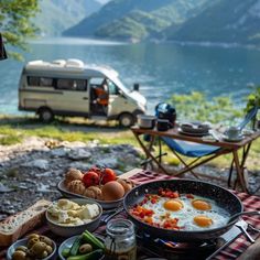 an outdoor table with food on it and a camper in the background