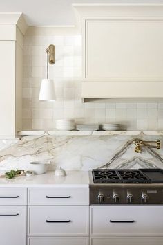 a kitchen with marble counter tops and white cabinets, along with brass pulls on the stove