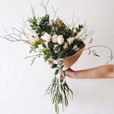 a person holding a bouquet of flowers with greenery on the stems and white roses