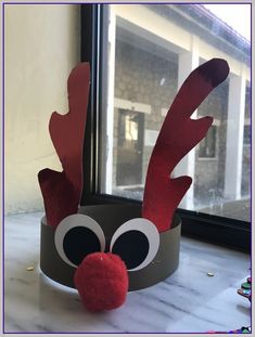 a paper crown with reindeer's nose and antlers on the top, sitting in front of a window