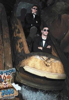 two men in suits and sunglasses are riding on an animal ride at the amusement park