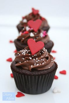 three cupcakes with chocolate frosting and sprinkles are on a white surface