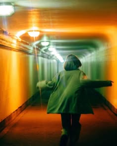 a woman in a green coat is walking down a long tunnel with her arms outstretched