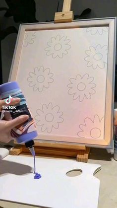 someone is painting flowers on a canvas with blue paint and a spray bottle in front of it