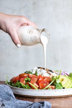 someone pouring dressing onto a salad with lettuce and tomatoes