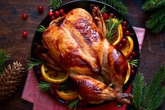 a roasted turkey on a platter with oranges, pine cones and cranberries