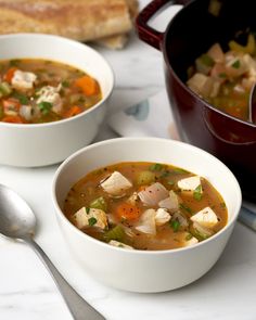 two bowls of soup on a table with silverware and bread in the back ground